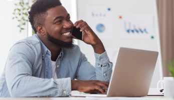 Cheerful man sat in front of his laptop and speaking on the phone