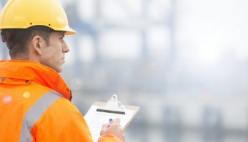 Man dressed in a high visibility jacket and a hard hat using a clipboard