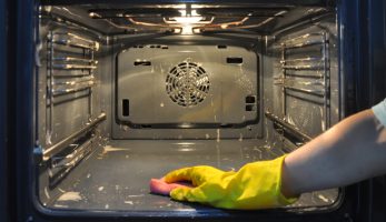 Man with yellow rubber gloves scrubbing the inside of an oven